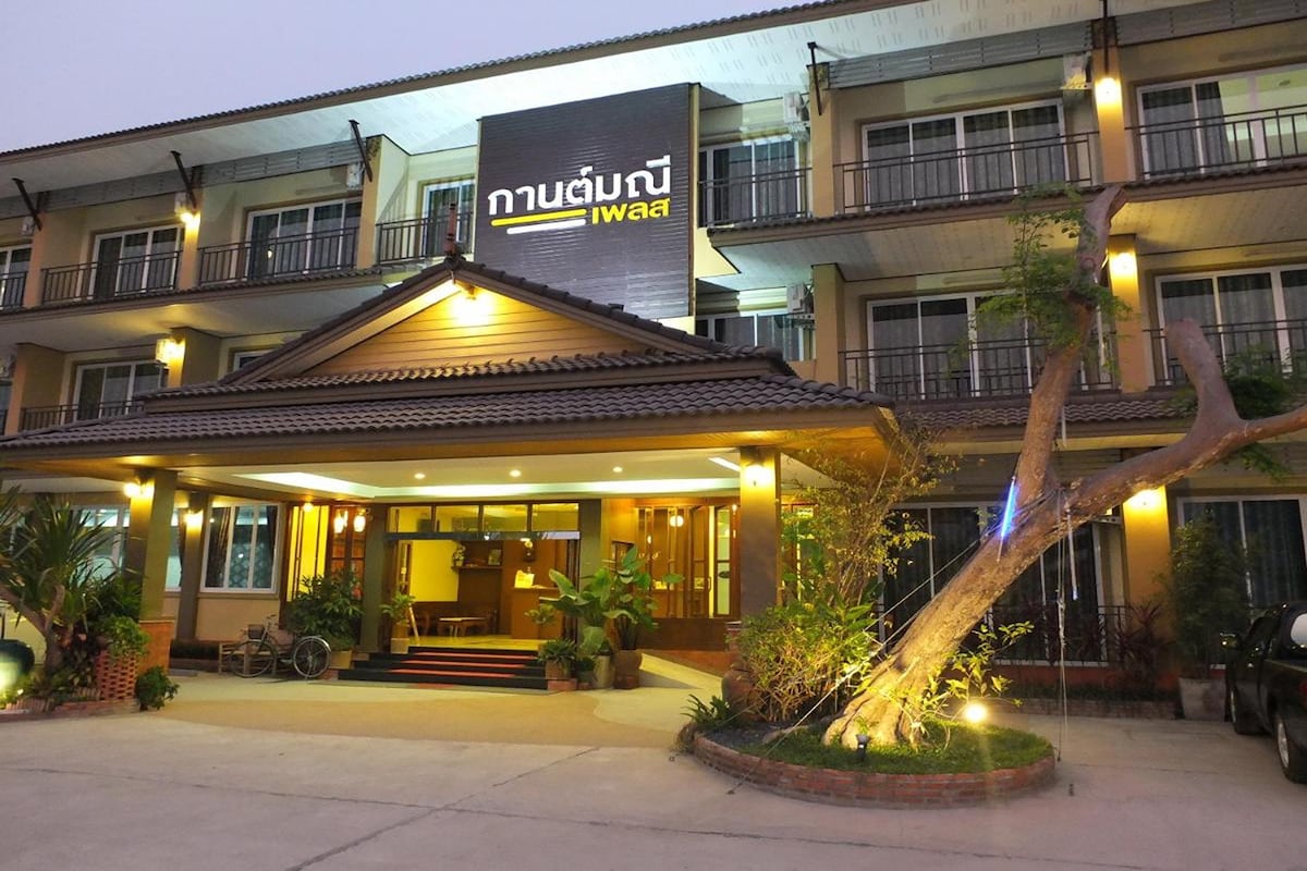 The exterior of the building showcases a blend of modern and traditional architecture, highlighted by warm lighting. A welcoming entrance with plant accents leads to a spacious lobby area, while upper-level balconies offer a view of the surrounding environment.