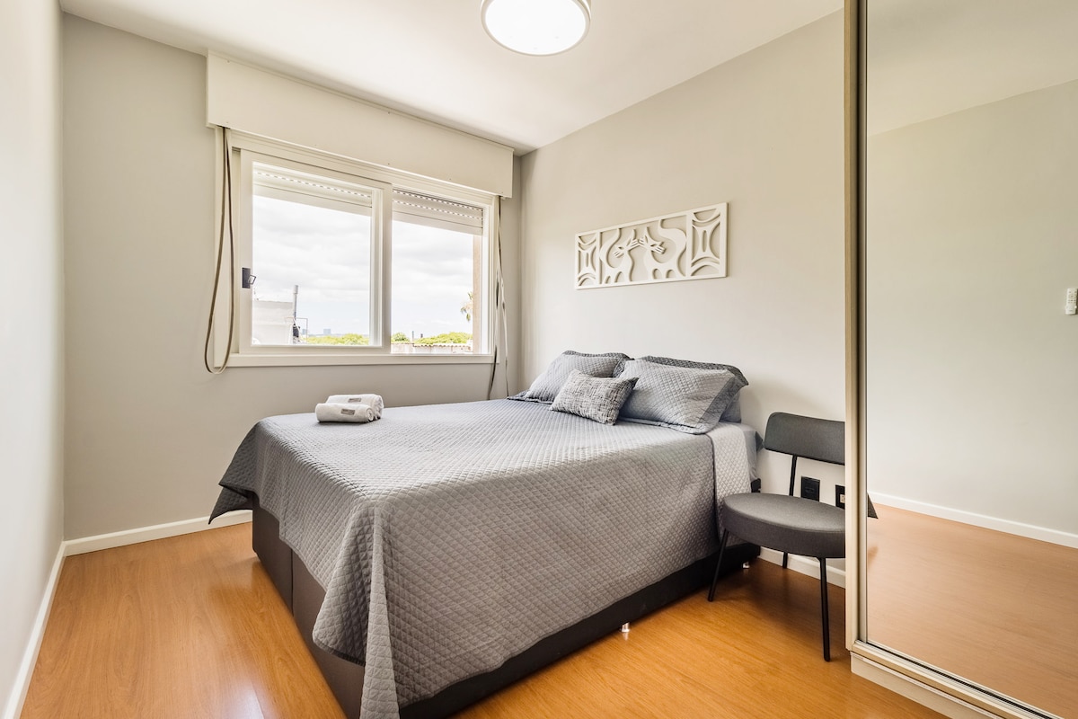 Slaapzaal met comfortabel queensize bed, krachtige plafondventilator met afstandsbediening, kledingkast met spiegeldeuren, raam met jaloezie.