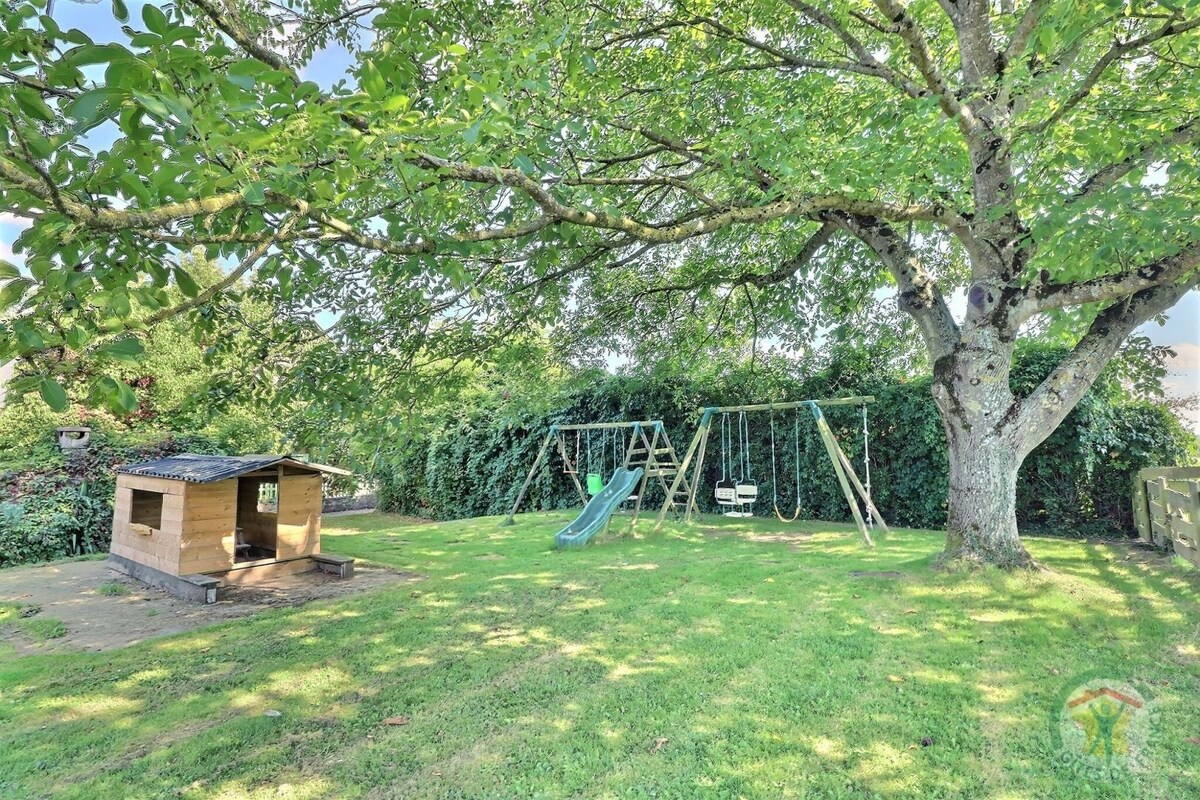 A spacious outdoor area is highlighted by a large tree providing shade. A wooden playhouse is visible alongside a swing set, which includes a slide. The lawn is well-maintained, creating an inviting space for outdoor activities.