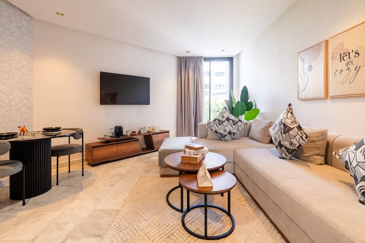 Dnevni boravak ispunjen svjetlošću s modularnim kaučem, ukrasnim jastucima i stolićima koji se mogu slagati jedan u drugi. Veliki prozor sa zavjesama za zamračivanje. Smart TV (Netflix) s niskom medijskom jedinicom. Blagovaonski kutak na lijevoj strani; glatki prijelaz u spavaću sobu i na terasu.