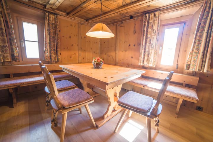 Tradicionalna blagovaonica u engadinskom salonu s antiknim drvenim namještajem, udobnom kutnom klupom i dva šarmantno integrirana jednostruka kreveta – idealno za obitelji ili dodatne goste.

