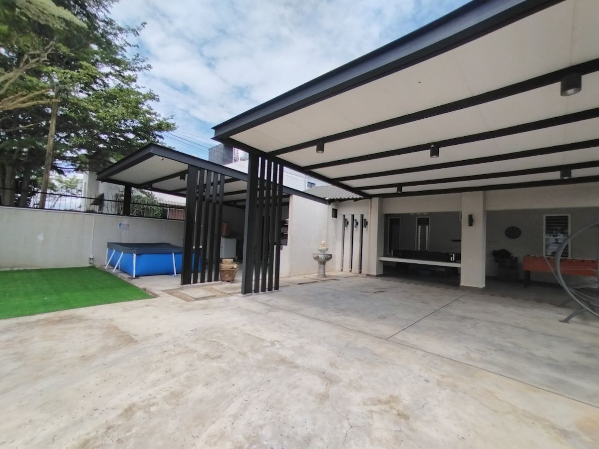 An expansive outdoor area is visible, featuring a swimming pool and a concrete patio. Modern architectural lines are highlighted by black support beams. A playful green patch of grass adds a vibrant touch, while a sleek water feature enhances the tranquil ambiance.