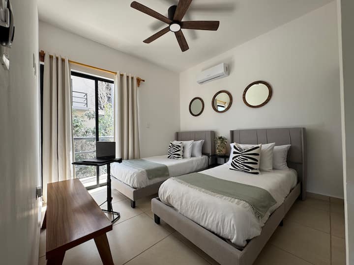 Მეორე საძინებლის ხედი ორი კომფორტული ორადგილიანი საწოლით, ლეპტოპის სადგამით, კარადათი და ცალკე აივნით.