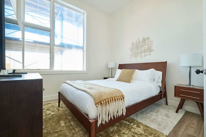 Dormitorio principal luminoso con una cama tamaño queen, detalles acogedores y grandes ventanales que dejan entrar la luz natural, creando un refugio relajante.