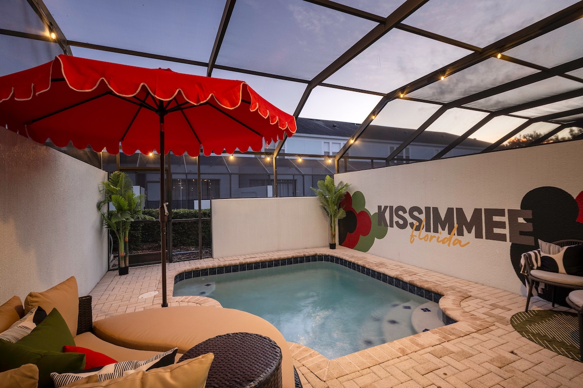A private heated plunge pool is surrounded by a screened enclosure, ensuring safety and comfort. Colorful outdoor furniture invites relaxation, while a vibrant umbrella provides shade. The wall features a playful design, adding a touch of whimsy to the outdoor space.