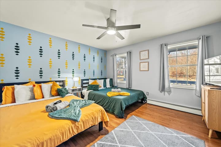 Тази оживена спалня се отличава с игрив, модерен дизайн на стената със смесица от зелени и жълти акценти. С две удобни легла, вентилатор на тавана за прохладен бриз и много естествена светлина, това е идеалното място за почивка и релаксация.