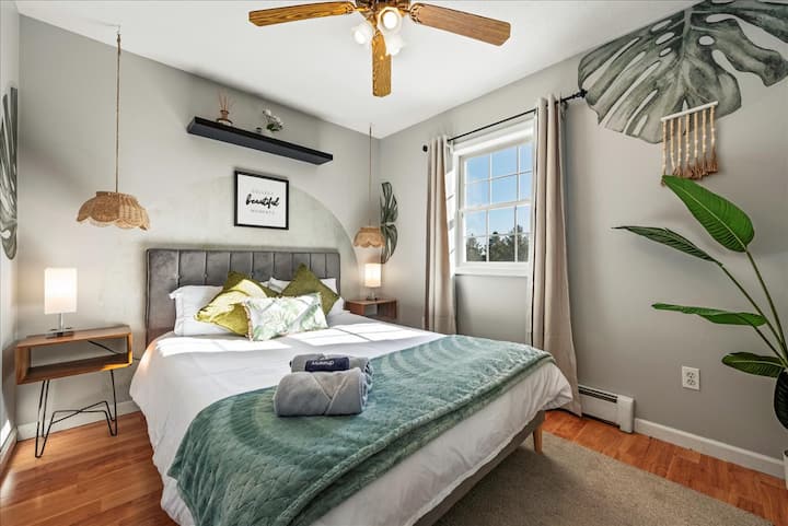 Тази уютна спалня се отличава с успокояваща тематика, вдъхновена от природата, с меки зелени тонове, ботанически акценти и минималистична естетика. Смесица от модерни мебели, игриво стенно изкуство и естествена светлина създава спокойно, привлекателно място за отдих.