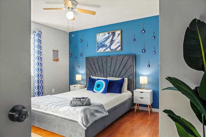 Тази ярка спалня се отличава с уникална тематика със сини акценти и символи, украсяващи стените, носещи усещане за защита и мистицизъм. Плюшеното легло и модерният декор създават спокойно и стилно пространство с културно значение.