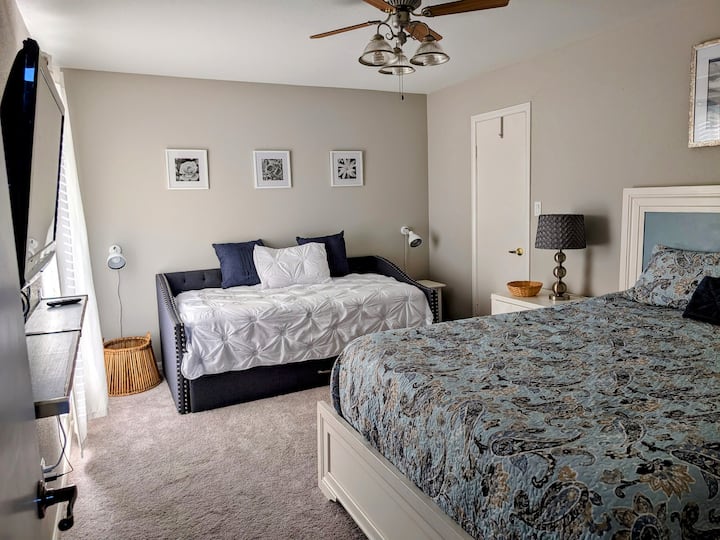 This room sleeps four with a queen bed featuring extra mattress toppers and a pull-out twin daybed with a hidden trundle underneath. There's a Roku TV, and the room offers ample space for luggage and movement. Extra-large closet for more storage.