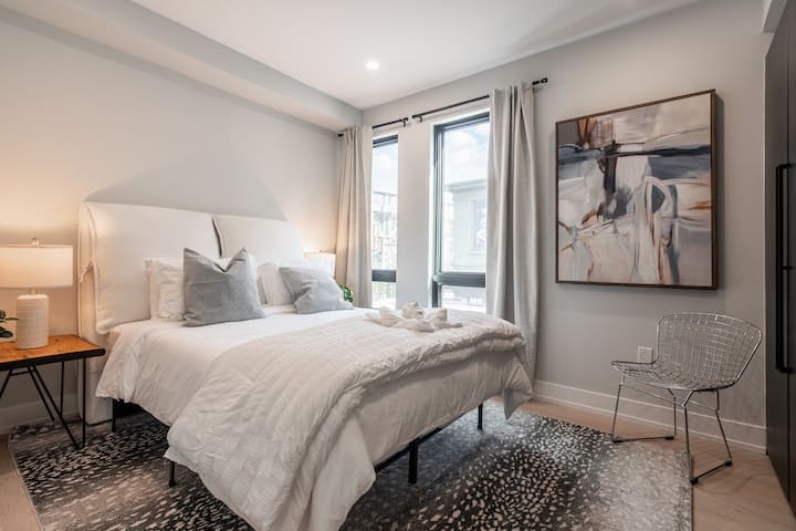 Svetlá a vzdušná spálňa s plyšovou čalúnenou manželskou posteľou, mäkkou posteľnou bielizňou a abstraktnými umeleckými dielami, ktoré vytvárajú pokojné útočisko.