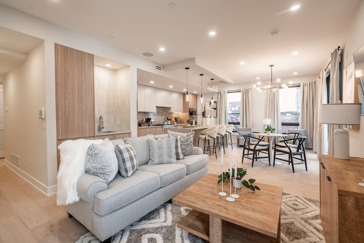 Svetlý a priestranný obývací priestor s modernými, štýlovými závesnými svetlami a útulným posedením – ideálne na oddych a zábavu.