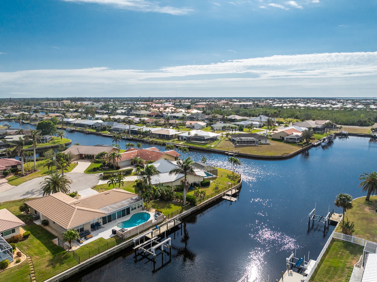 An aerial view showcases a serene canal surrounded by charming residential properties with well-maintained lawns. The image highlights tranquil water reflecting clear skies, enhancing the peaceful waterfront atmosphere of the area.