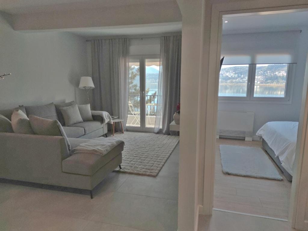 A modern living space features a comfortable gray sofa paired with a small side table. Natural light fills the room through a large window, offering a view of the serene surroundings. A soft area rug covers the floor, creating an inviting atmosphere.