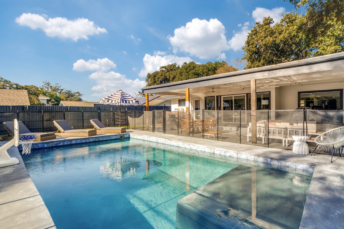 A private pool area is featured, showcasing a spacious rectangular pool with clear water. Comfortable lounge chairs are positioned on the surrounding patio, and a covered outdoor dining space is visible in the background, providing a shaded area for meals and relaxation.