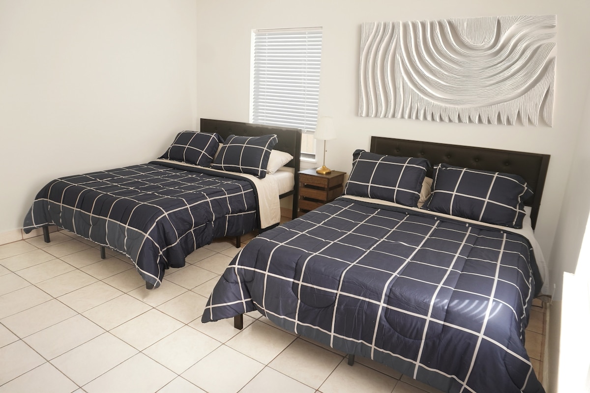 Amplio dormitorio con dos acogedoras camas dobles, complementado con ropa de cama elegante y una serena decoración de pared diseñada para tu ambiente de descanso.