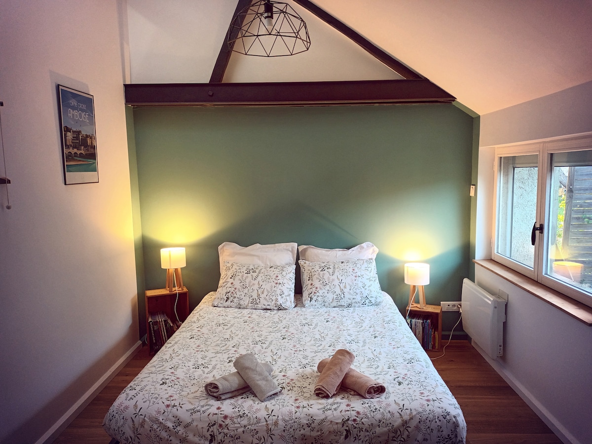 A cozy sleeping area is featured with a spacious bed adorned with floral bedding. Soft lighting from two bedside lamps enhances the warmth of the room. A window allows natural light, and books are neatly arranged on a shelf nearby.