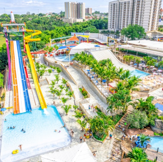 Aerial view of the Acqua Park shows vibrant water slides and a sprawling pool area. Lush greenery surrounds the space, while families enjoy various water attractions. Sun loungers and umbrellas are positioned around the pools, enhancing the inviting outdoor atmosphere.