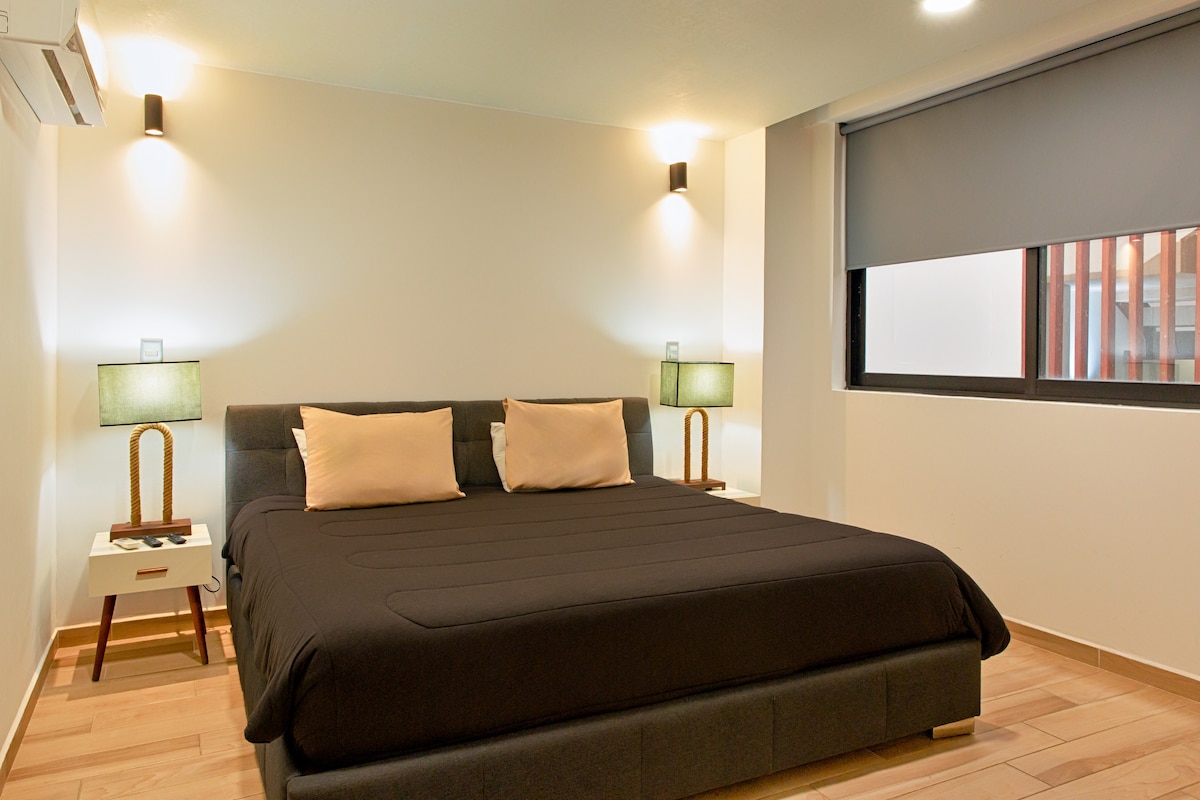 Ელეგანტური და მიმზიდველი საძინებელი — დიდი ზომის საწოლი თბილი განათებით, დამონტაჟებული სმარტ-ტელევიზორი, ხის თანამედროვე მოპირკეთება და პირადი სააბაზანო დამატებითი კომფორტისთვის და კომფორტისთვის