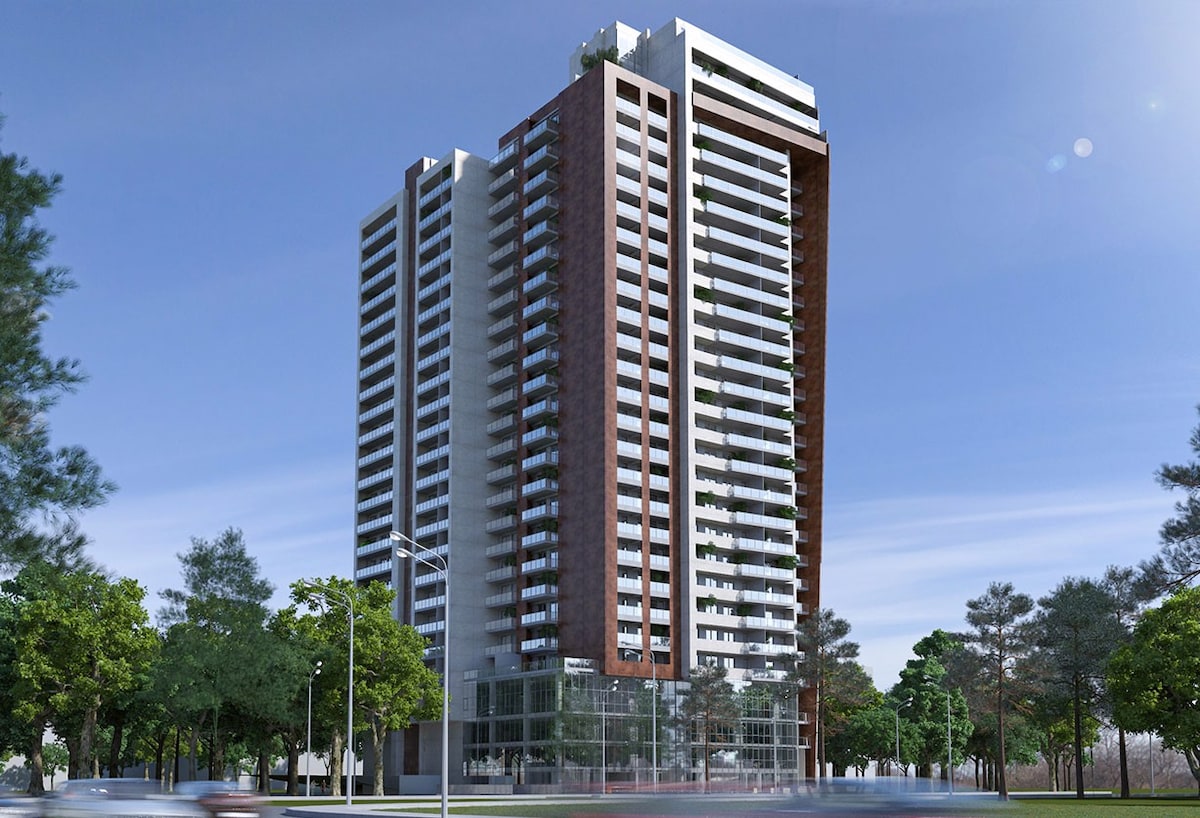 The image showcases the modern Archi Central Park Tower, a tall residential building featuring a mix of glass and steel facades. Lush greenery surrounds the base, while balconies extend from various levels. The sky is clear, highlighting the building's contemporary design against the natural landscape.