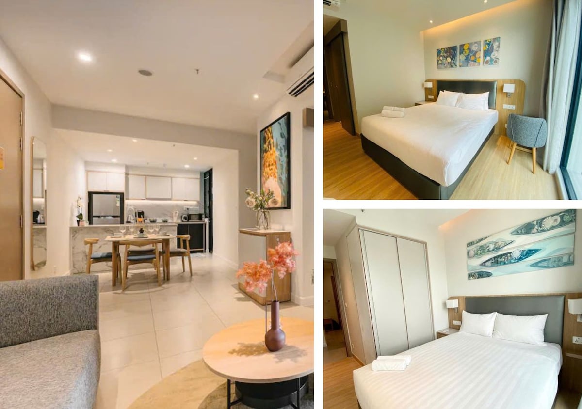 The spacious living area features a cozy sofa and a round coffee table beside vibrant decor. A well-equipped kitchen is visible in the background. The bedroom showcases a large bed with soft linens and elegant artwork. Ample natural light brightens the neutral-toned interiors.