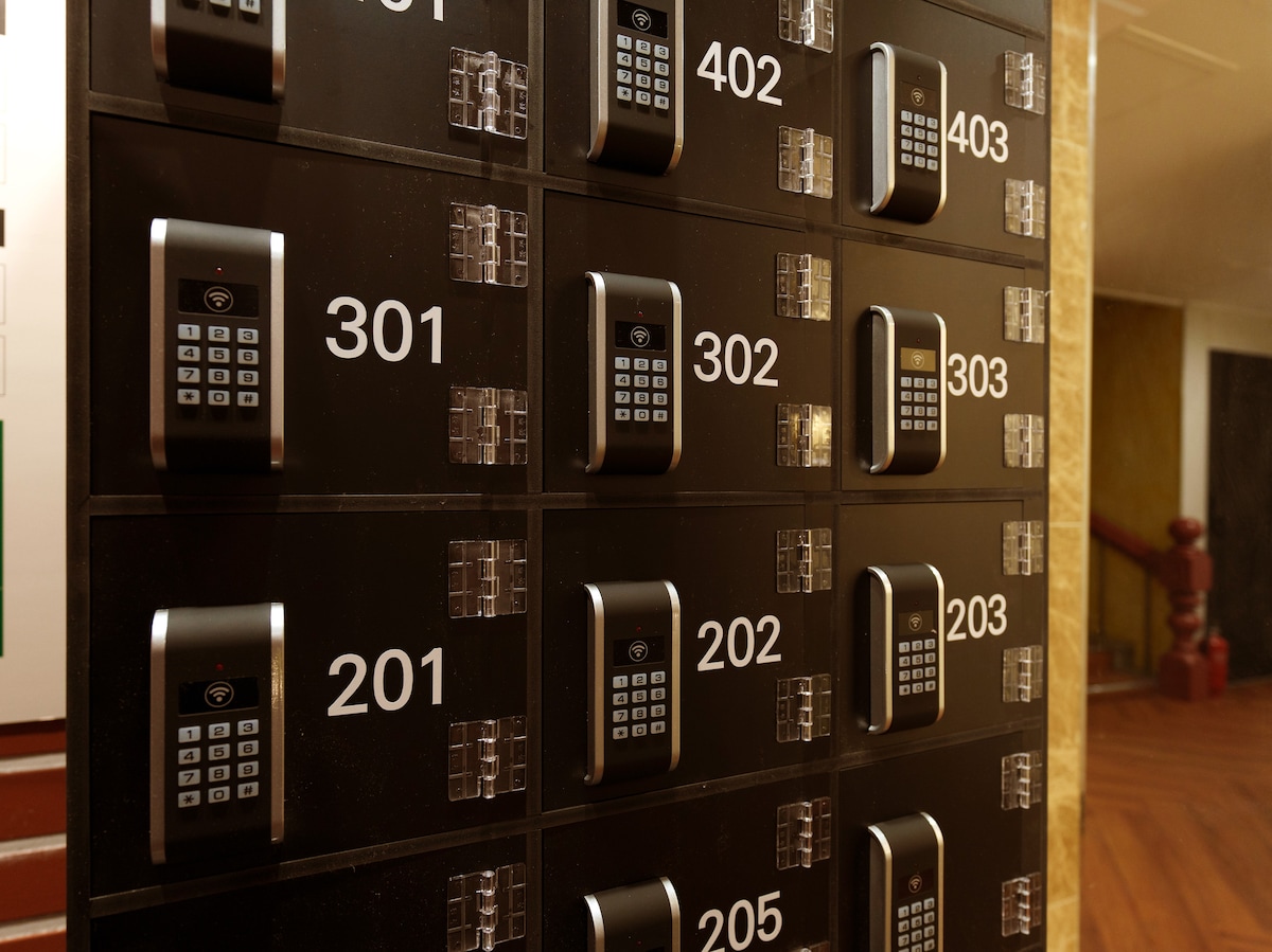 A wall-mounted keypad entry system is displayed, featuring a grid layout with several numbered compartments. Each compartment is equipped with a digital keypad, allowing for secure access. The dark surface of the system contrasts with light-colored walls nearby.