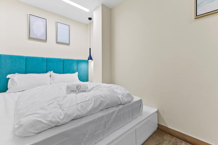 Un dormitorio acogedor con un cabecero turquesa, ropa de cama blanca y dos cuadros en la pared.