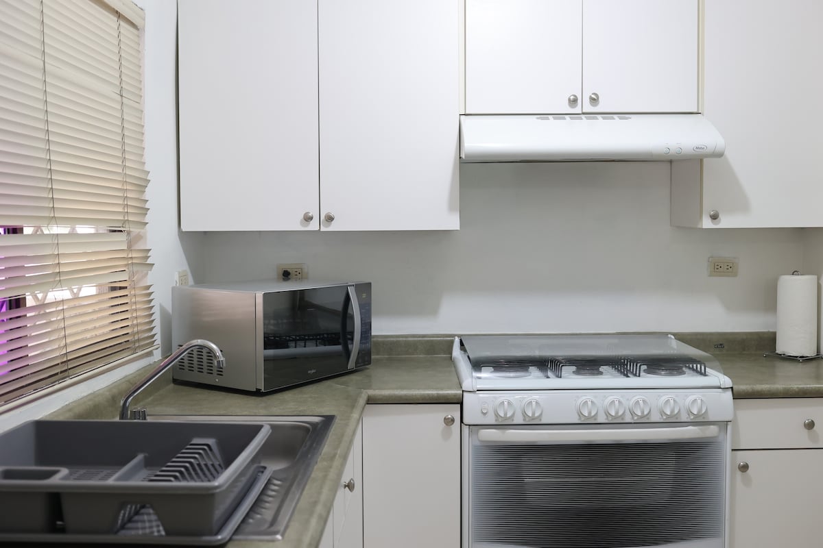 A modern kitchen is equipped with essential appliances, including a microwave and a stove with an exhaust hood. Light-colored cabinets provide storage, while a countertop offers space for food preparation. A sink and dish rack are situated on one side for convenience.