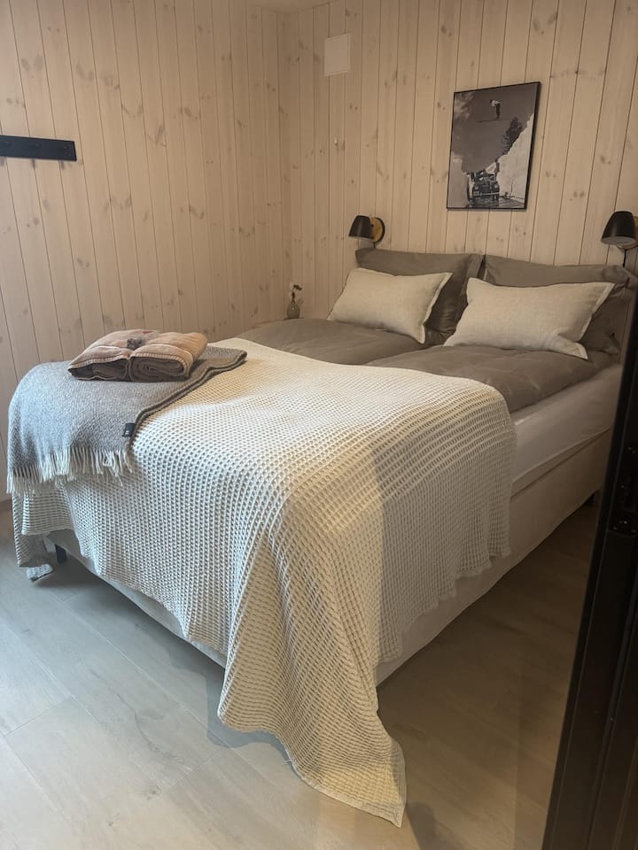 חדר שינה עם מיטה נוחה, שולחן ליד המיטה ותאורת לילה רכה.