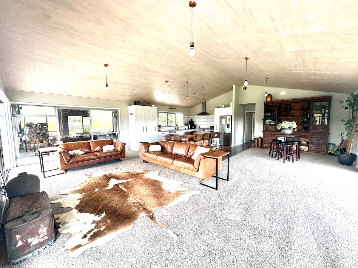 An open living area features two comfortable leather sofas, a dining table for family gatherings, and a well-equipped kitchen. Natural light floods the space through large windows, illuminating the plush carpet and complementing the warm tones of the decor.