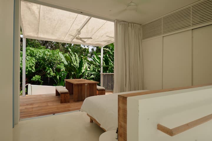 Bezproblémové bývanie v interiéri – spálňa sa otvára na bujnú zelenú terasu s dreveným jedálenským kútom, ktorá ponúka dokonalú kombináciu súkromia a prepojenia s prírodou.
