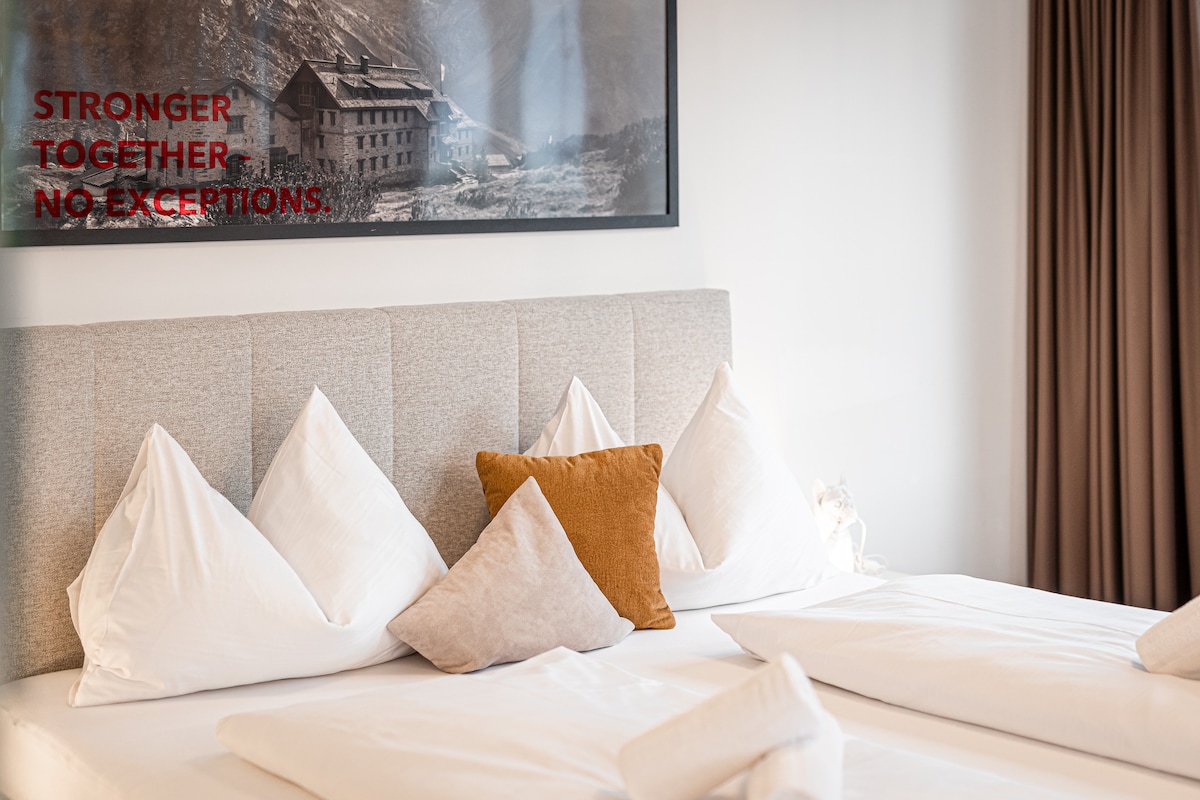 The sleeping area features a spacious bed with light-colored bedding and a variety of decorative pillows, including a brown one. A large framed black-and-white landscape photograph adorns the wall above the bed, complemented by soft, warm lighting from a nearby source.