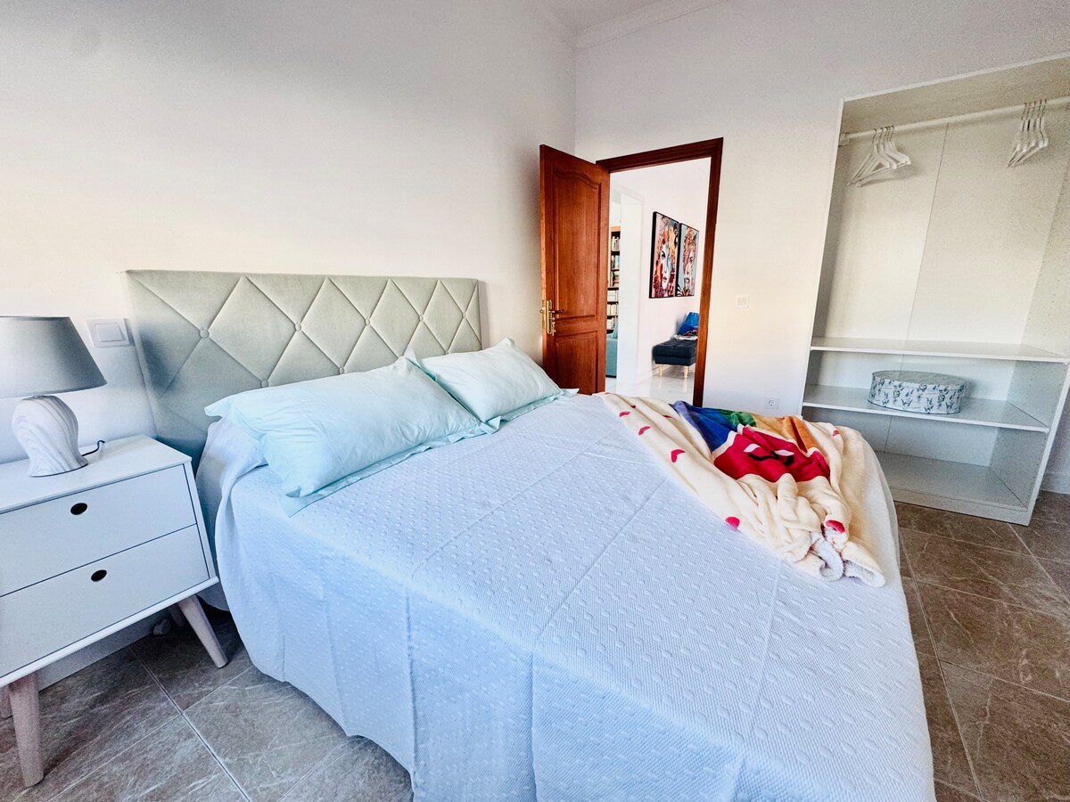 ห้องนอนพร้อมเตียง 150 หน้าต่างด้านนอกมองเห็นทางเข้าผ้าห่มทึบแสงและพัดลมเพดาน 
ห้องนอนพร้อมเตียงควีนไซส์หน้าต่างทางเข้าหลักม่านม้วนและพัดลมเพดาน 