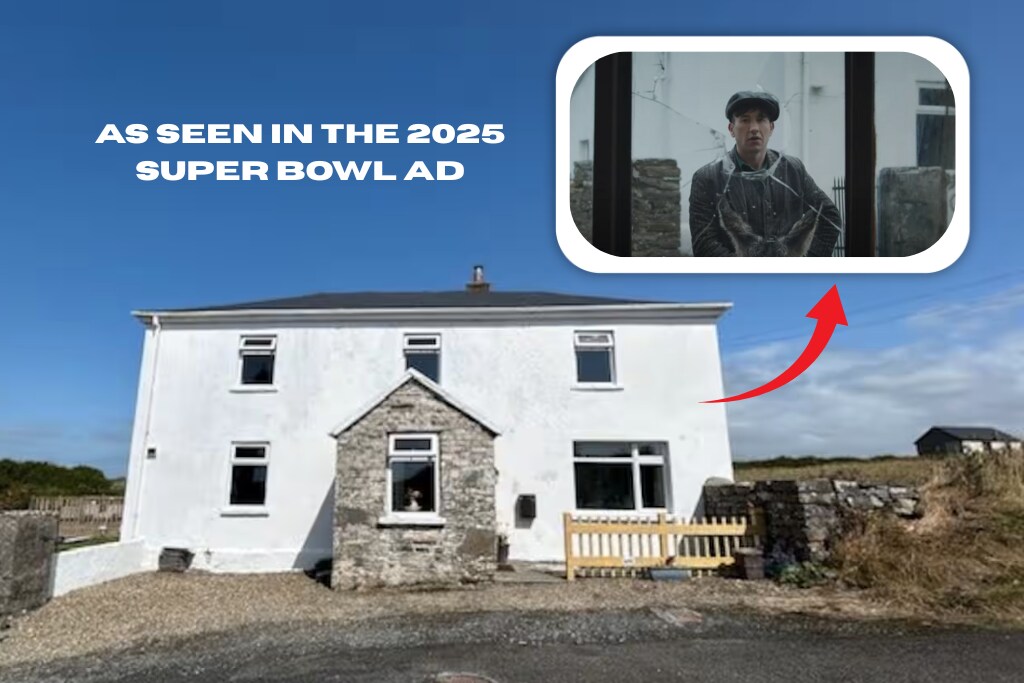 The exterior of a traditional two-story house is visible, featuring a combination of white walls and stone accents. A fenced area is located at the front, while large windows reflect the clear blue sky, suggesting a welcoming entrance. The location is highlighted for its connection to a recent Super Bowl advertisement.