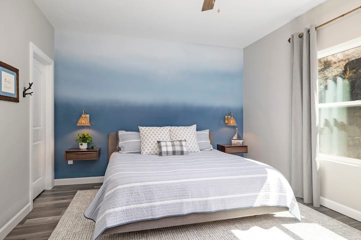 Отпуснете се със стил в тази спокойна кралска спалня с успокояваща акцентна стена, вдъхновена от езерото Омбре, плюшени възглавници и уютно спално бельо. Затъмнените завеси осигуряват спокоен сън, докато вградените нощни шкафчета и топлото осветление добавят както функция, така и чар.