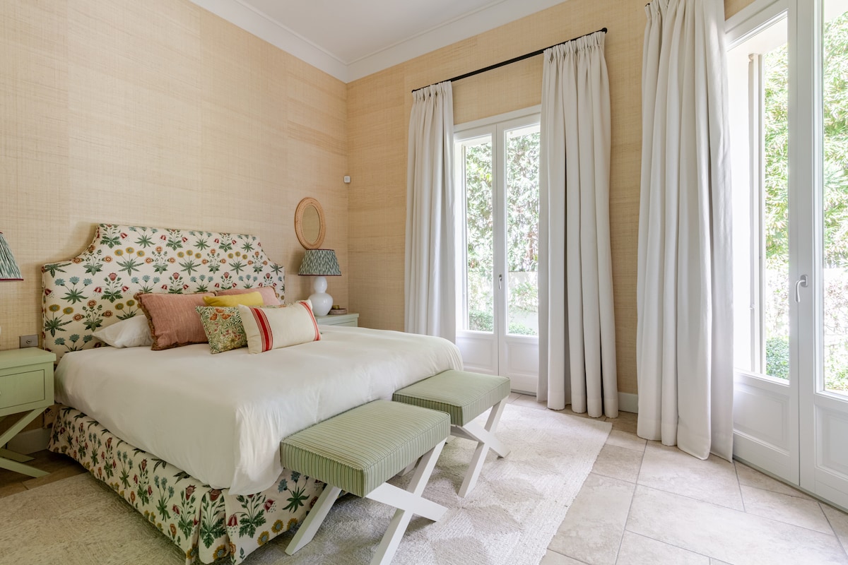 Elegant and tranquil guest double bedroom with soft neutral tones, a comfortable bed, large windows with garden views, and direct access to ample storage. A peaceful retreat filled with natural light.