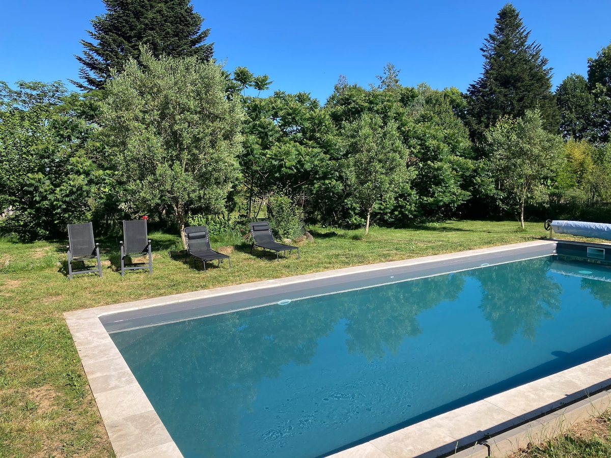 A tranquil eco-pool reflects the clear blue sky, surrounded by lush greenery. Four lounge chairs are positioned nearby on neatly trimmed grass, inviting relaxation and enjoyment of the natural setting.