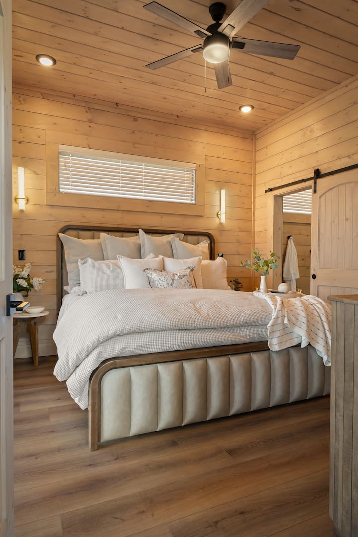Master bedroom offers a true retreat with a luxurious king-size bed, plush bedding, & an inviting, serene atmosphere. Sliding doors provide direct access to the balcony, blending indoor comfort with peaceful outdoor views. Located on the main level.