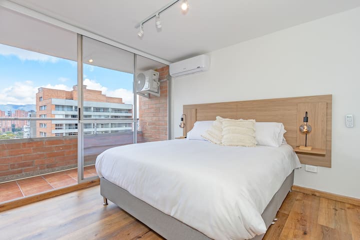 Svetlá izba s manželskou posteľou a veľkými oknami s výhľadom na mesto. Jeho minimalistický dizajn a teplé povrchové úpravy vytvárajú dokonalú atmosféru na oddych.