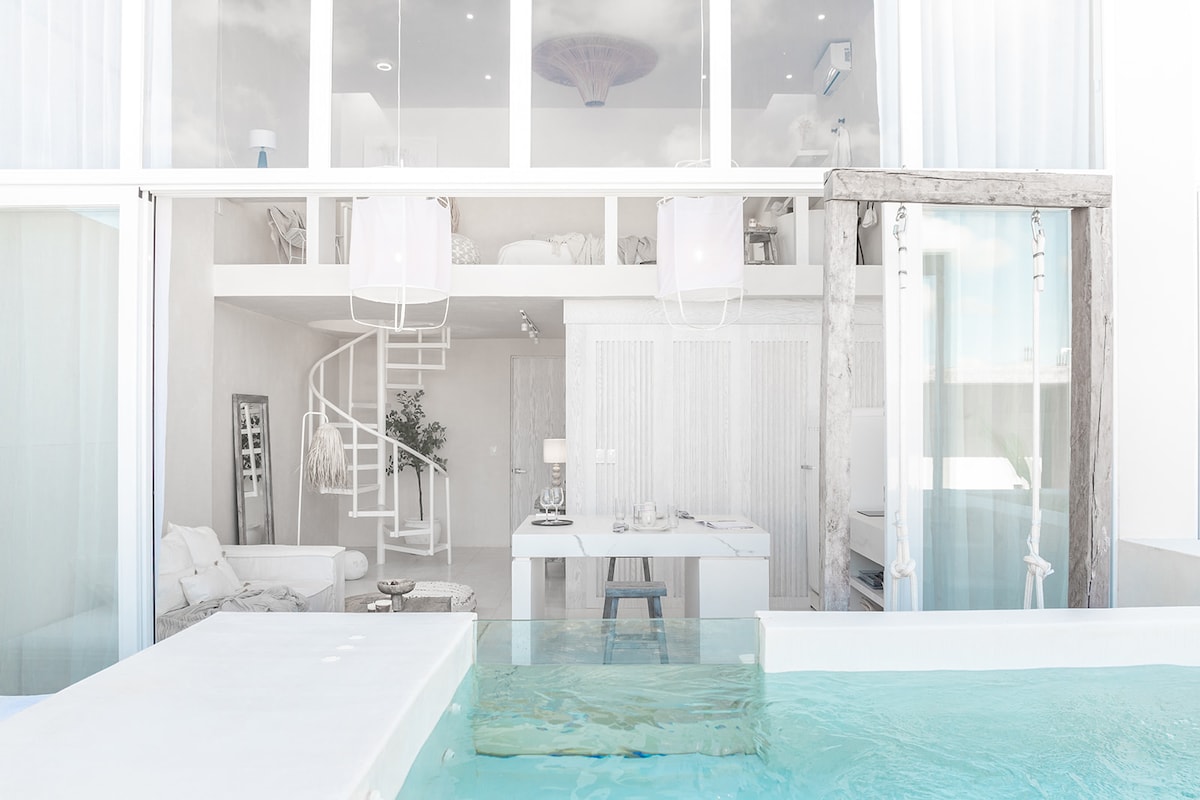 A modern open-plan area features a sleek dining space, complemented by a spiral staircase leading to an upper level. Large glass windows invite natural light, while a serene pool area extends outside, creating a seamless connection between indoor and outdoor living.