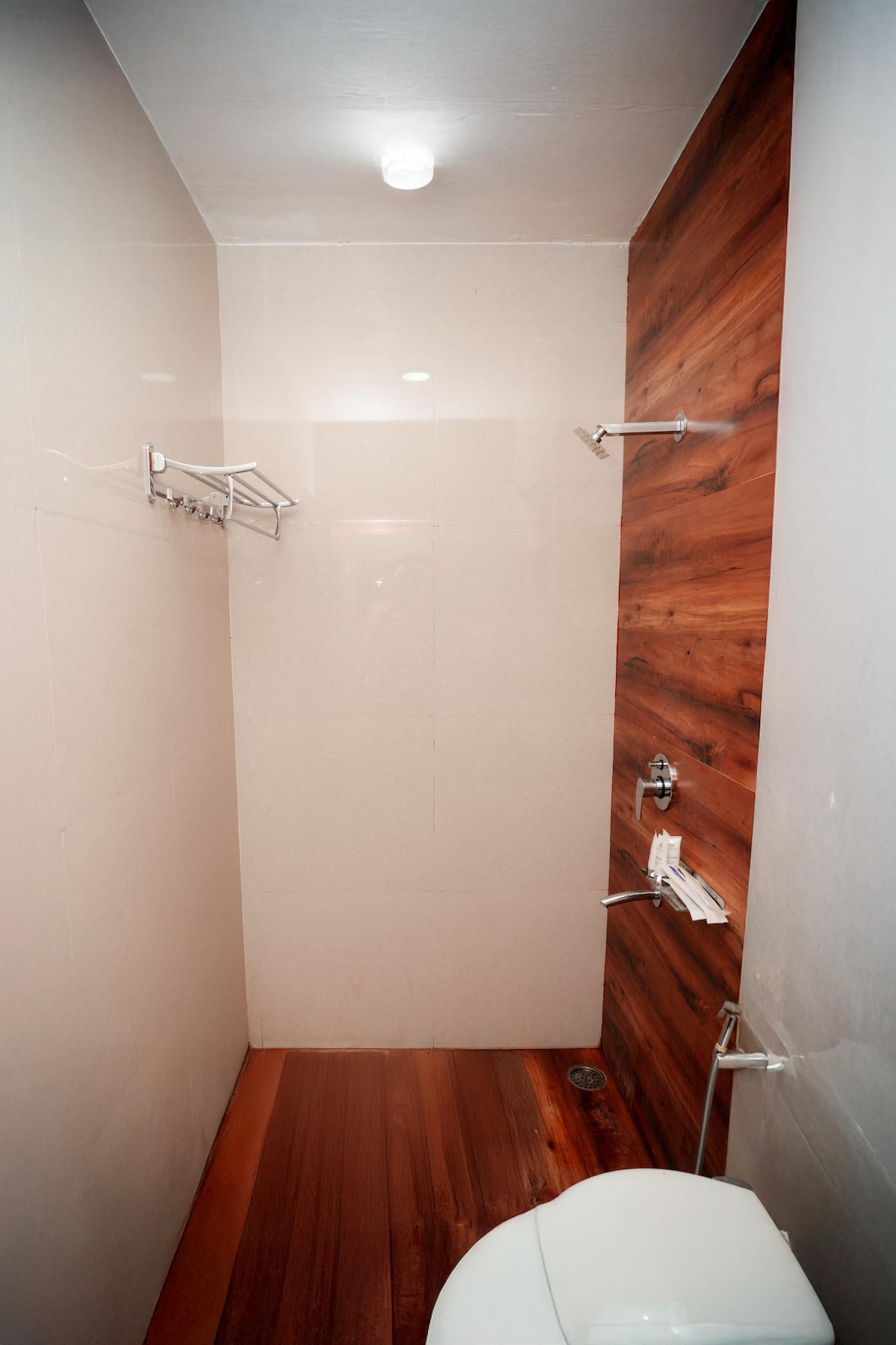 A clean and modern bathroom features a combination of tile and wooden accents. Minimal fixtures include a wall-mounted towel rack and a sleek shower area. The space is well-lit with a ceiling light, enhancing visibility in the neutral-toned environment.