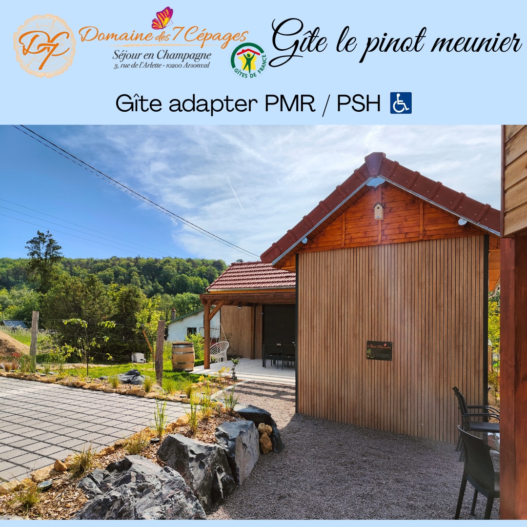 A modern gîte with a wooden exterior is featured, showcasing a sloped roof and large entrance. A paved pathway leads to the entrance, bordered by landscaped rocks and greenery. Accessibility features are highlighted for individuals with mobility needs.