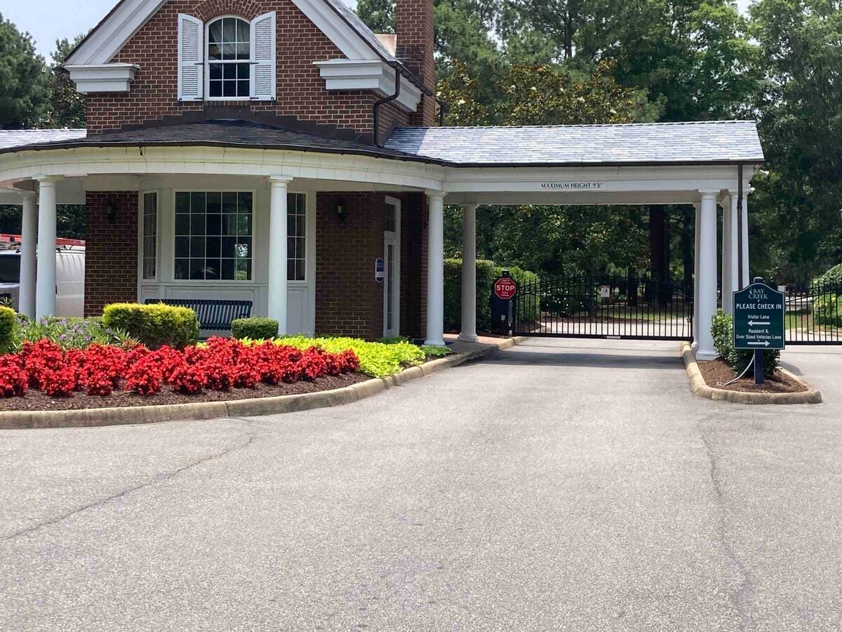 A well-maintained entrance welcomes visitors with a neatly landscaped pathway featuring vibrant red and yellow flower beds. The building showcases a classic brick design, complete with large windows and a covered entryway. A security gate is visible in the background, enhancing guest privacy.