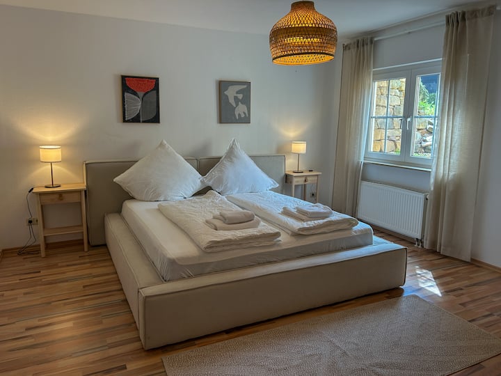 Helles Schlafzimmer mit gemütlichem Kingsize-Bett (1,80 × 2,00 m), stilvoll eingerichtet und mit viel Tageslicht. Ideal zum Erholen nach einem schönen Tag in der Umgebung.