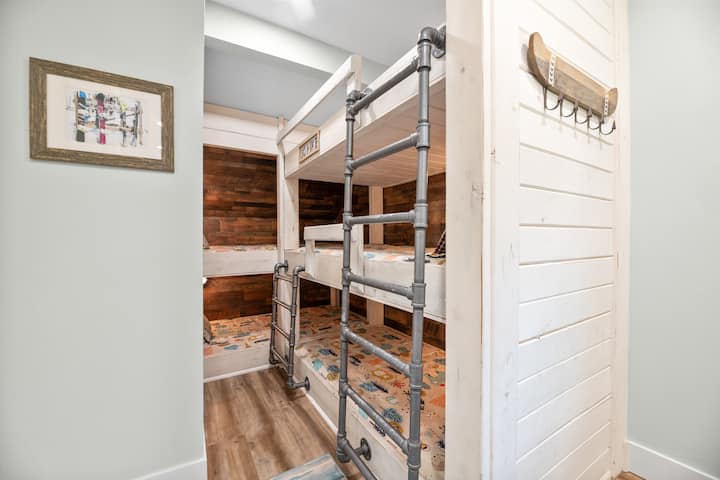 This upper level bedroom has 2 bunk beds with a total of 5 twin beds. The first bunk bed has 2 stacked beds. The second bunk bed has 3 stacked beds. It has a sitting area with hardwood floor, loveseat, Sonos sound system, & 45” Samsung TV with Roku.