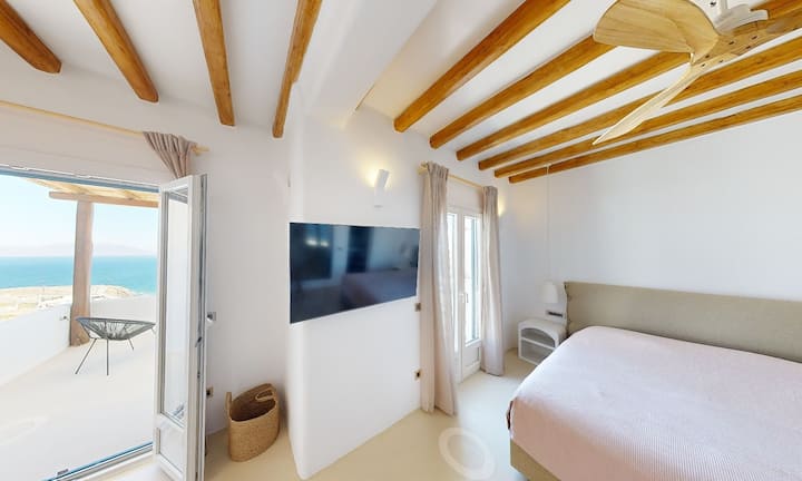 חדר שינה זוגי בקומה הראשונה עם מאוורר תקרה מעוצב, פינת הלבשה, טלוויזיה חכמה, חדר רחצה מודרני ומרפסת פרטית עם נוף מדהים לים.