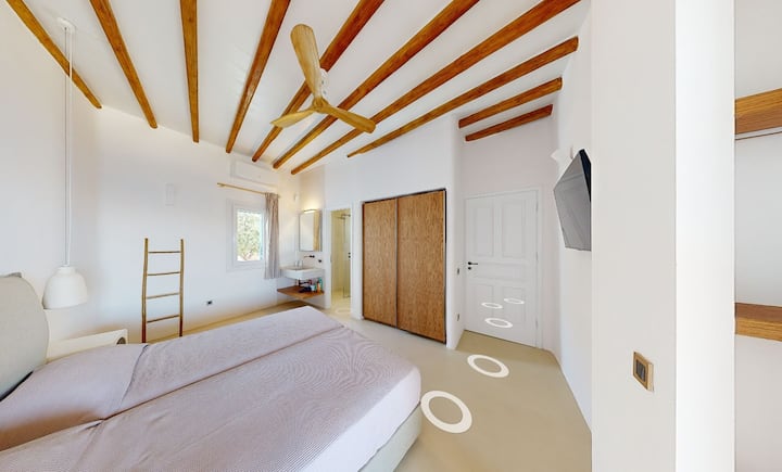 חדר שינה זוגי בסוויטה בקומה הראשונה עם טלוויזיה חכמה, מאוורר תקרה, ארון גדול, חדר רחצה מודרני, מרפסת פרטית עם נוף לים וגישה ישירה לאזור הבריכה.