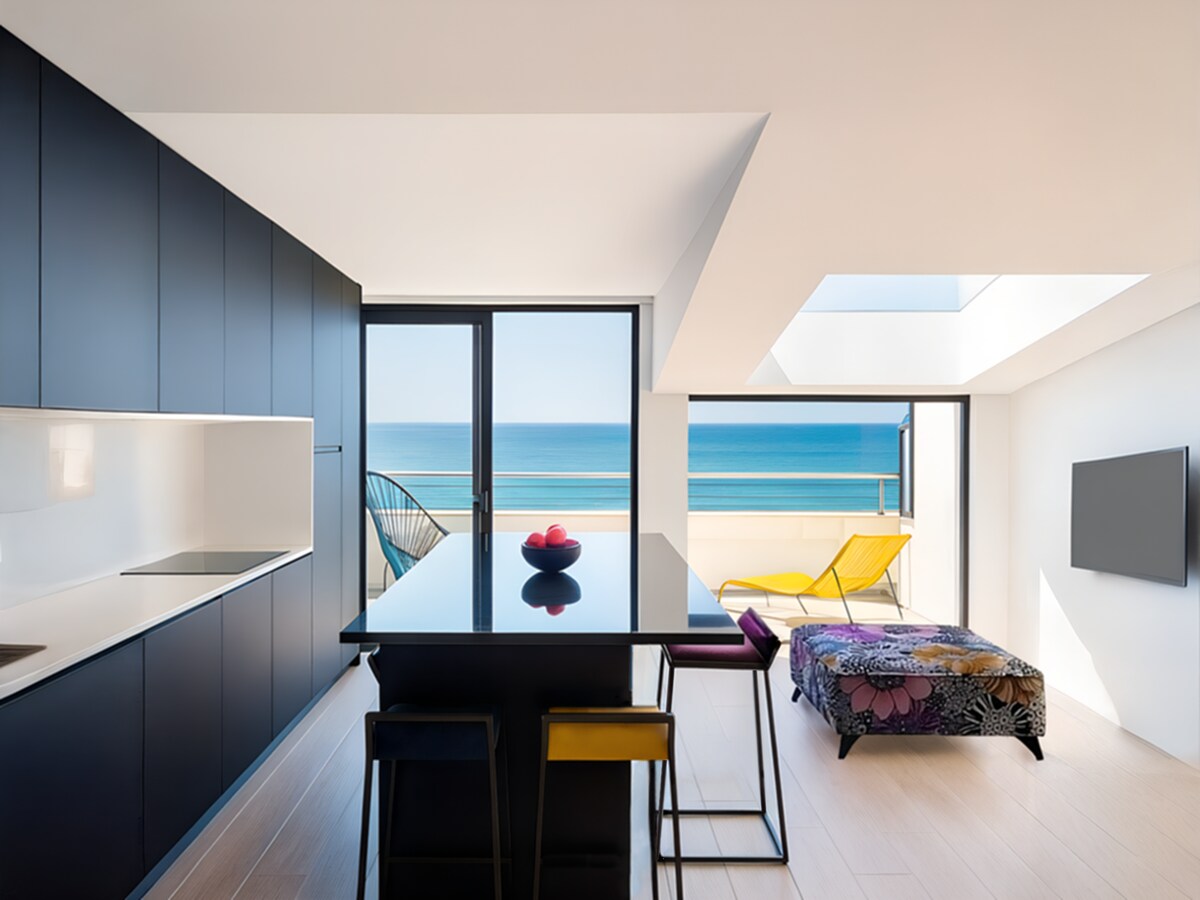 A modern kitchen area features sleek black cabinetry and a central island with bar stools. Large windows provide an unobstructed view of the ocean, while a lounge area with a colorful sofa and a yellow chair creates a vibrant space filled with natural light.