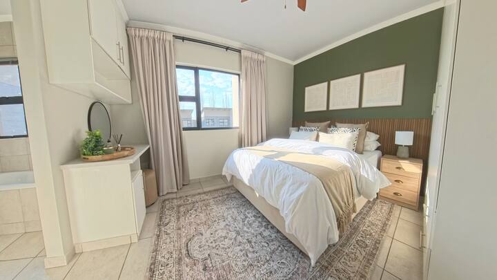 Cómodo dormitorio con baño privado con una cama tamaño queen extra larga, sábanas y toallas 100 % de algodón. Esta habitación también incluye un tocador con espejo y secador de pelo, perchero, calefacción, ventilador de techo, armarios empotrados con perchas y cortinas 100 % opacas.