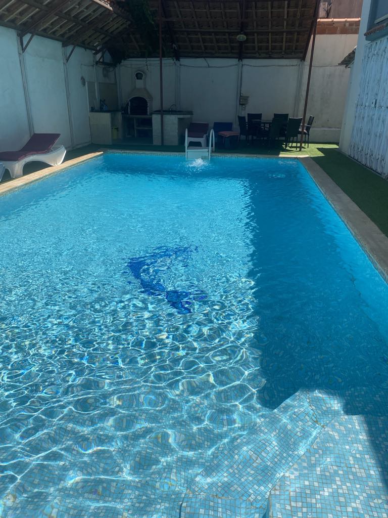 A private swimming pool is showcased, featuring clear blue water reflecting sunlight. Poolside seating is available with lounge chairs arranged beside the water. A shaded outdoor dining area with a table and chairs is positioned nearby, inviting relaxation.