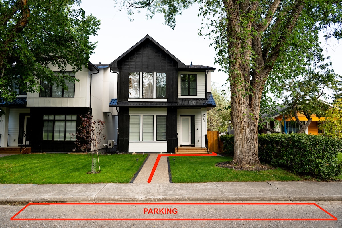 A modern two-story house features a distinctive black exterior and a well-maintained front yard with green grass. A clear path leads from the street to the entrance, with free street parking visible nearby. Trees provide a natural border to the property.